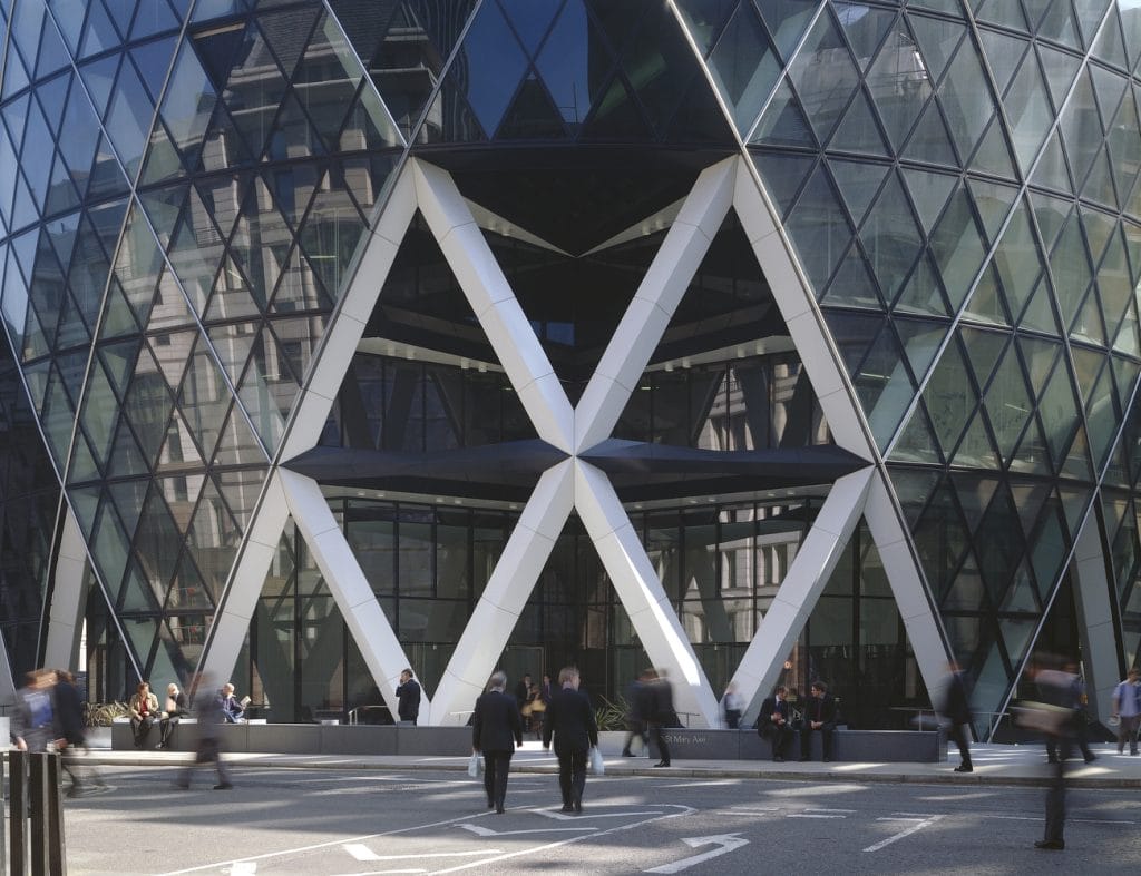 People walking outside the glass and steel entrance of a modern, distinctive office building with a geometric facade, known for its diamond-shaped window patterns and innovative use of aluminium in modern architecture.
