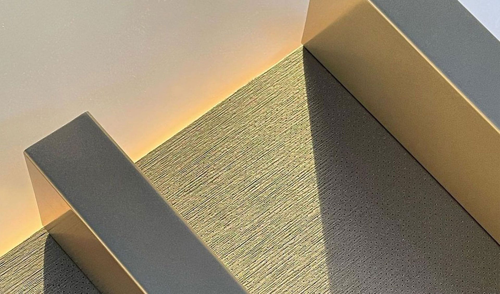 Sunlight casts geometric shadows on a modern staircase with textured steps and smooth railings, creating a minimalist and abstract pattern with soft yellow lighting on the wall.