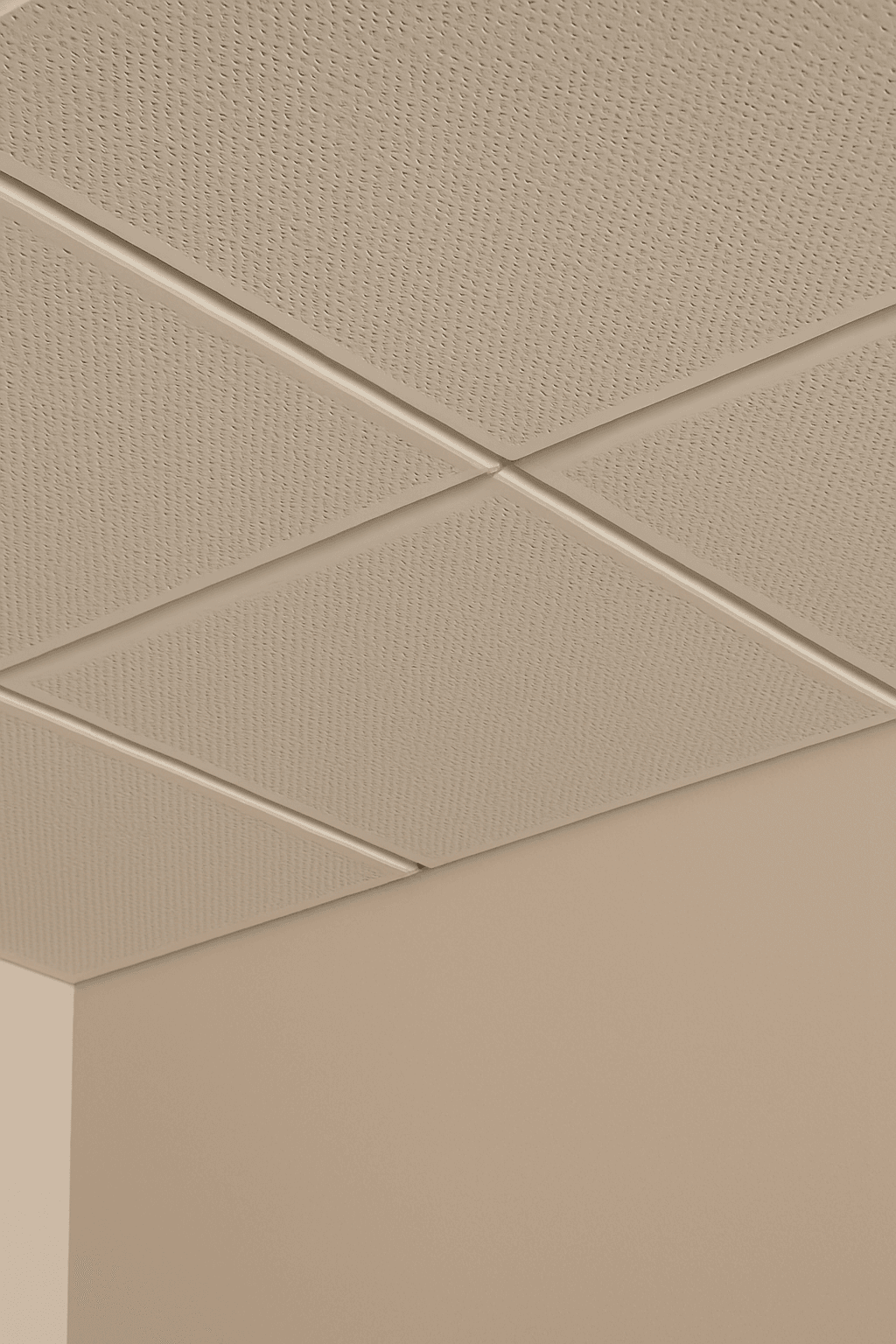 A beige drop ceiling with textured acoustic tiles in a grid pattern above a cream-colored wall corner.