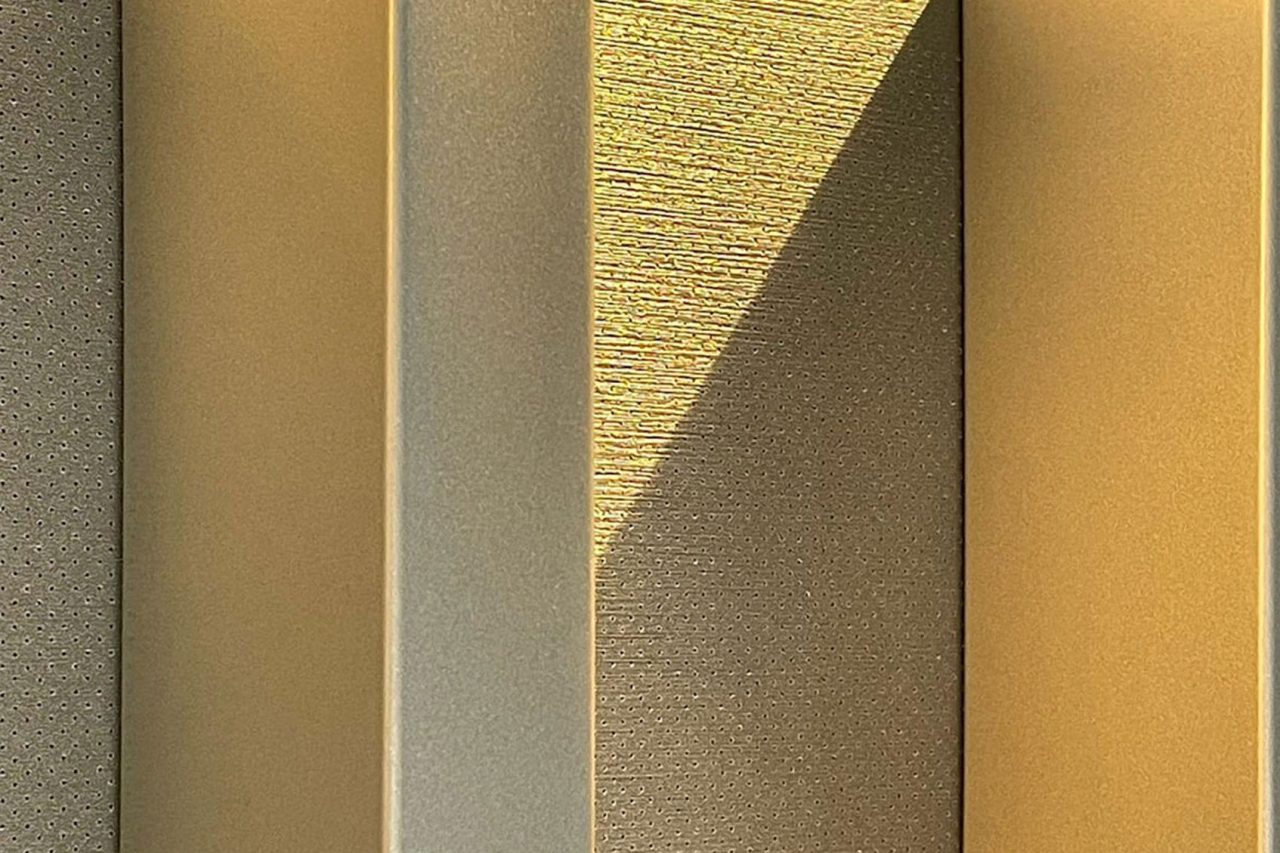 Close-up of vertical metallic panels with a textured surface, illuminated by warm sunlight casting shadows and highlighting the golden tones and patterns on the surfaces.