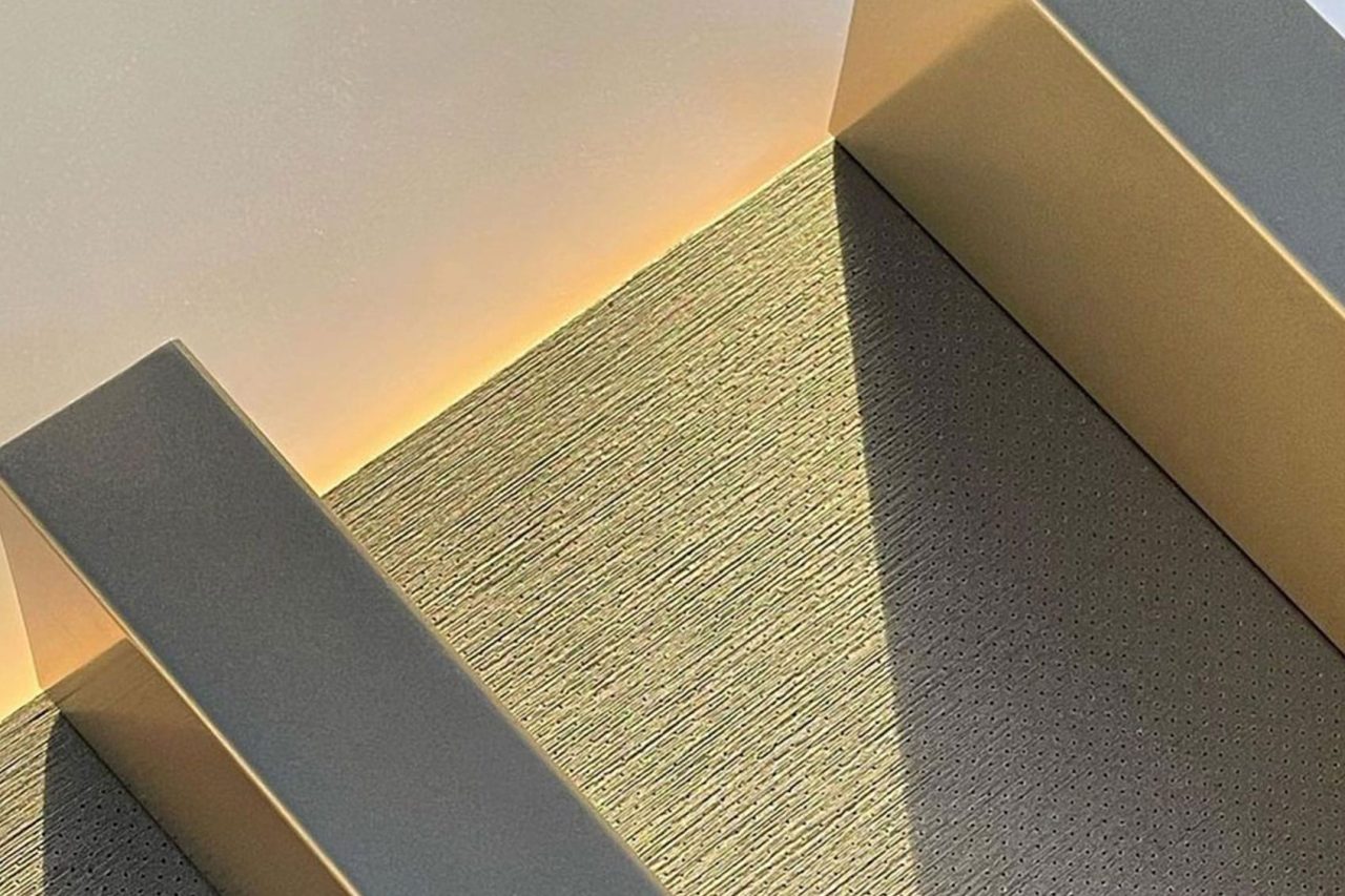 Sunlight casts geometric shadows on a modern staircase with textured steps and smooth railings, creating a minimalist and abstract pattern with soft yellow lighting on the wall.