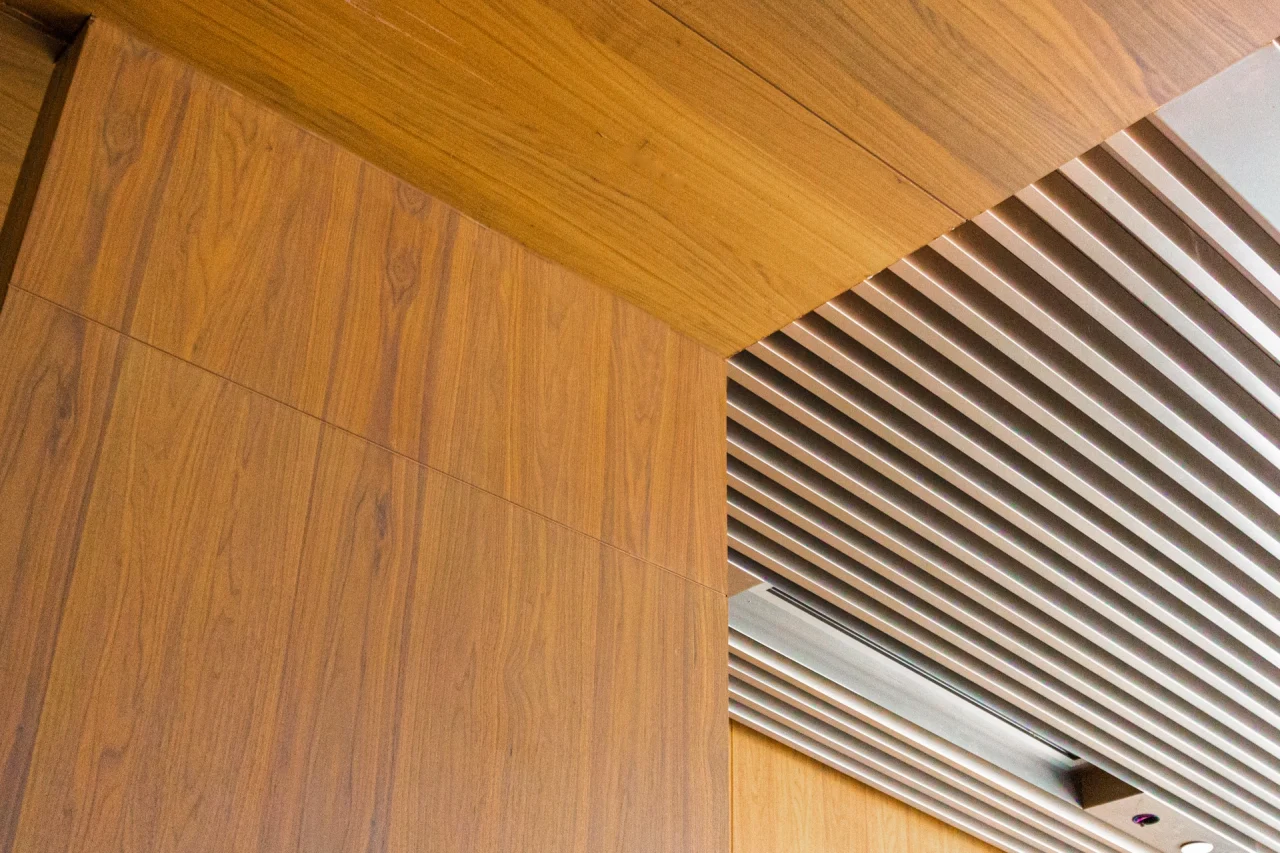 A modern ceiling design featuring vertical wood paneling on the left and a section with parallel metallic slats on the right, creating a geometric pattern with contrasting materials.